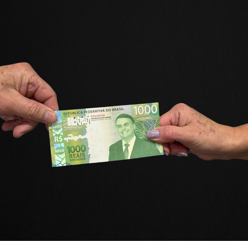 Duas pessoas trocando a Cédula Colecionável Bolsonaro de mão sobre uma mesa de madeira
